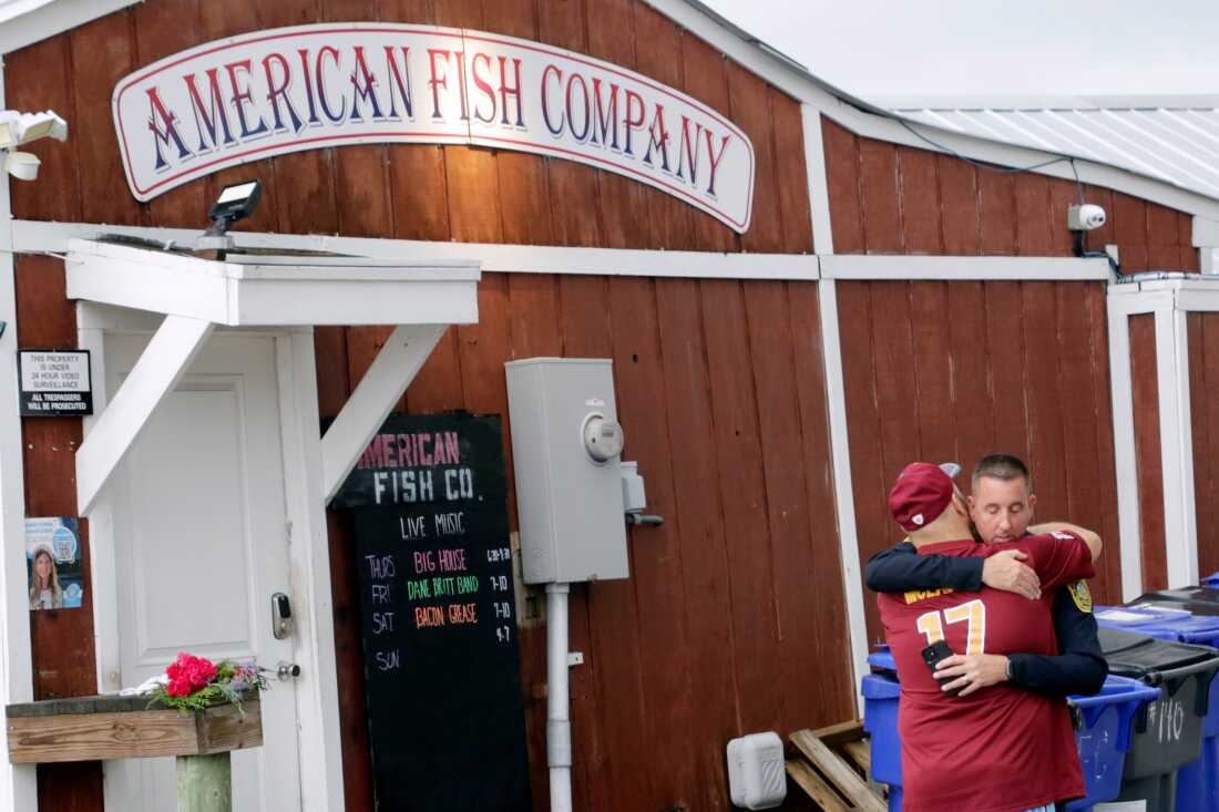 A man hugs a police officer in front of the American Fish Company following a fatal shooting that occurred the night before, on Sunday in Southport, N.C.