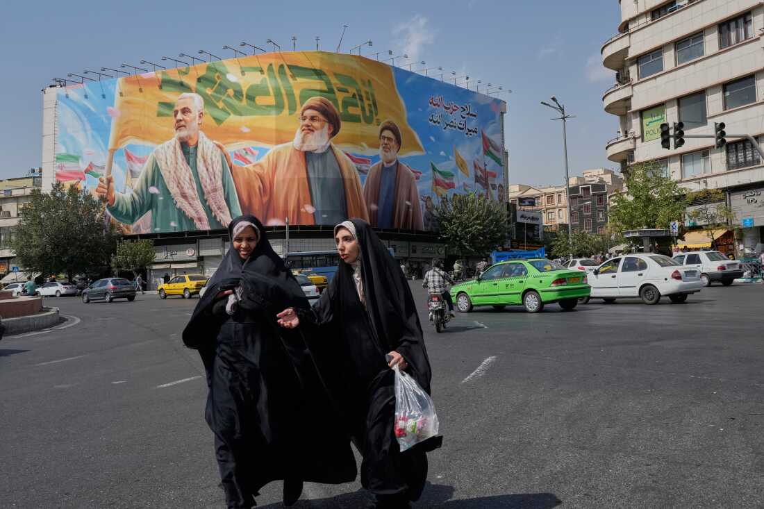 Two women walk past a huge banner showing the late commander of the Iran's Revolutionary Guard expeditionary Quds Force, Gen. Qassem Soleimani, who was killed in a U.S. drone attack in 2020, and two late Hezbollah leaders Hassan Nasrallah, center, and Hashem Safieddine, who were killed in Israeli airstrikes in 2024, at the Enqelab-e-Eslami (Islamic Revolution) square, in Tehran, Iran, Saturday, Sept. 27, 2025.