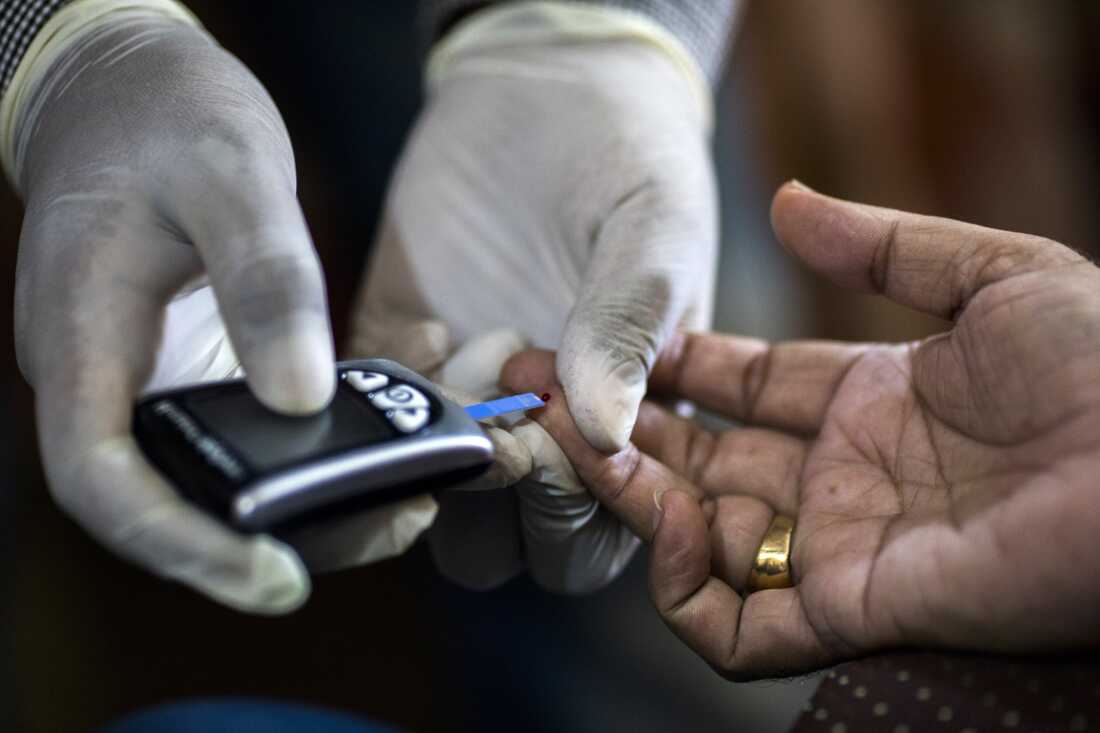 With gloved hands, a Public Health Foundation of India worker pricks a patient's finger while conducting a blood glucose test during a free door-to-door screening program in India's Haryana state.