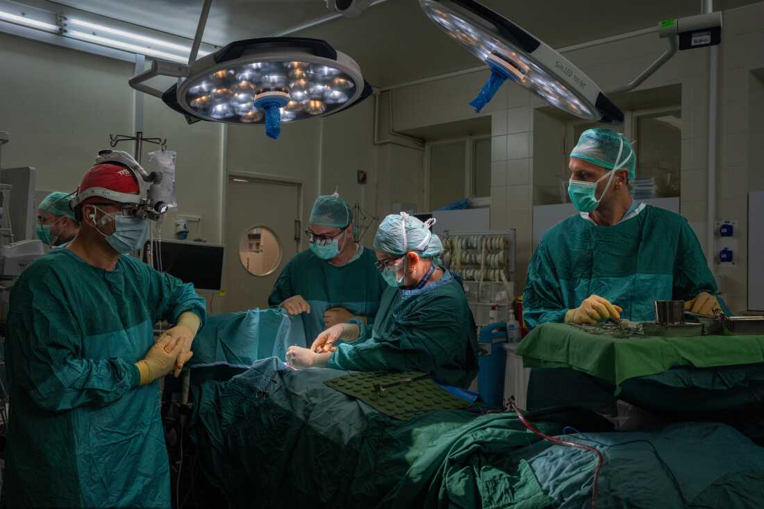Medical workers surround a patient lying on a table in an operating room.
