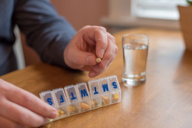 Man using a pill holder for daily meds, vitamins and supplements (Picture: Getty Images)
